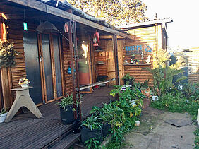 The picture shows the newly build Workshop, lots of green plants in the foreground and individual details on the construction itself, e. g. shelfs, decoration, tools, ... 