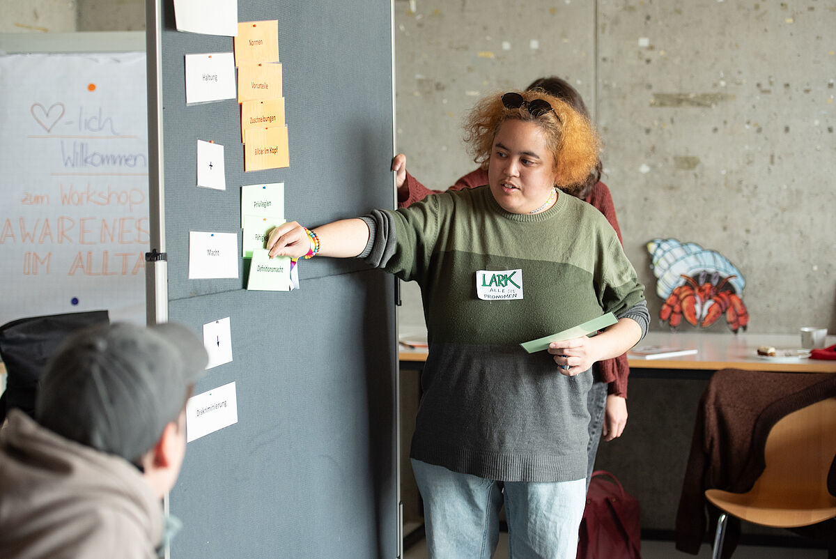 Eine Person pinnt eine Notiz an eine Pinnwand während des Workshops „Neurodiversität, Mad Pride & Co – Wer bestimmt, was normal ist?“.
