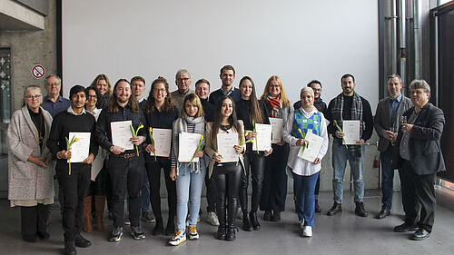 Gruppenbild, auf dem im Vordergrund nebeneinander die ausgezeichneten Studierenden mit Urkunden in den Händen zu sehen sind.